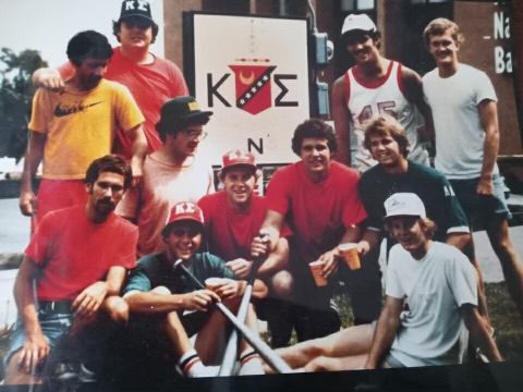 Brothers in T-shirts and caps gathered in front of a Kappa Sigma sign