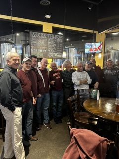 Alumni brothers, several in maroon, standing together in a brewery taproom
