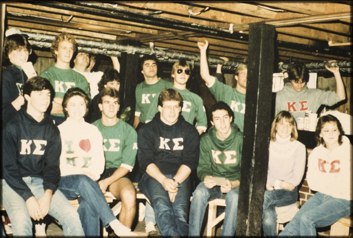 A large group in Kappa Sigma shirts seated on benches in a wood-framed room