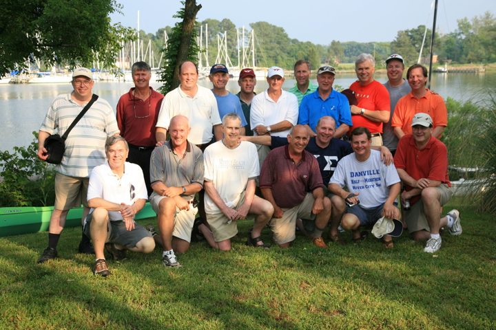 Brothers gathered on a lawn by the water with boats behind them